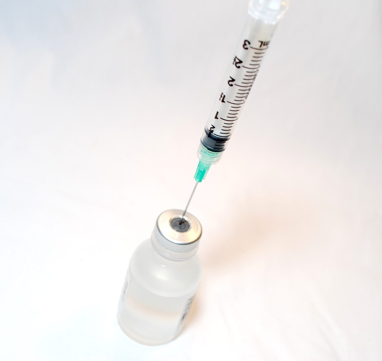 A syringe drawing liquid from a vaccine vial
